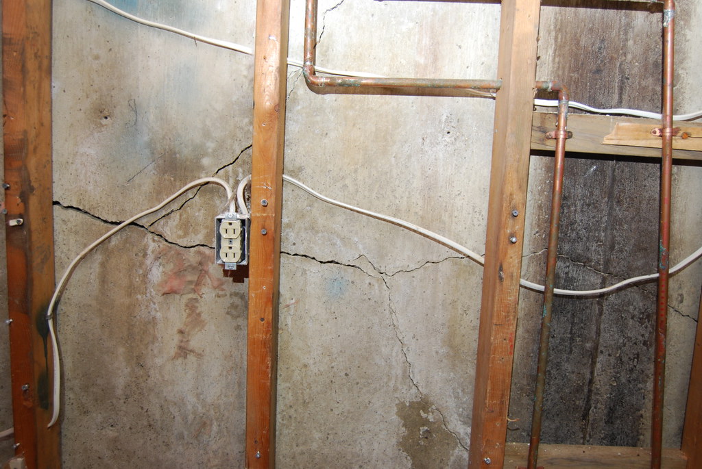 Long crack running across a basement foundation wall behind exposed framing